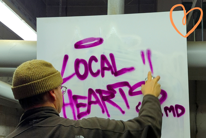 Digitales Engagement bei Local Hearts Magdeburg - Ein Mann besprüht ein Plakat mit Schrift "Local Hearts"